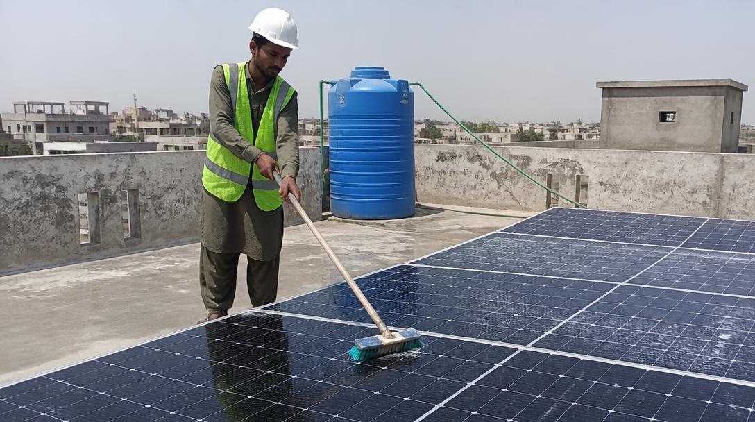 Pakistani technician cleaning rooftop solar panels on a flat concrete roof
